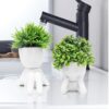 White ceramic human-style planters holding lifelike artificial succulents for interior design.