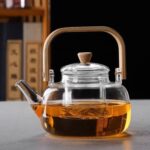 Clear borosilicate glass teapot with infuser and wooden handle on white background